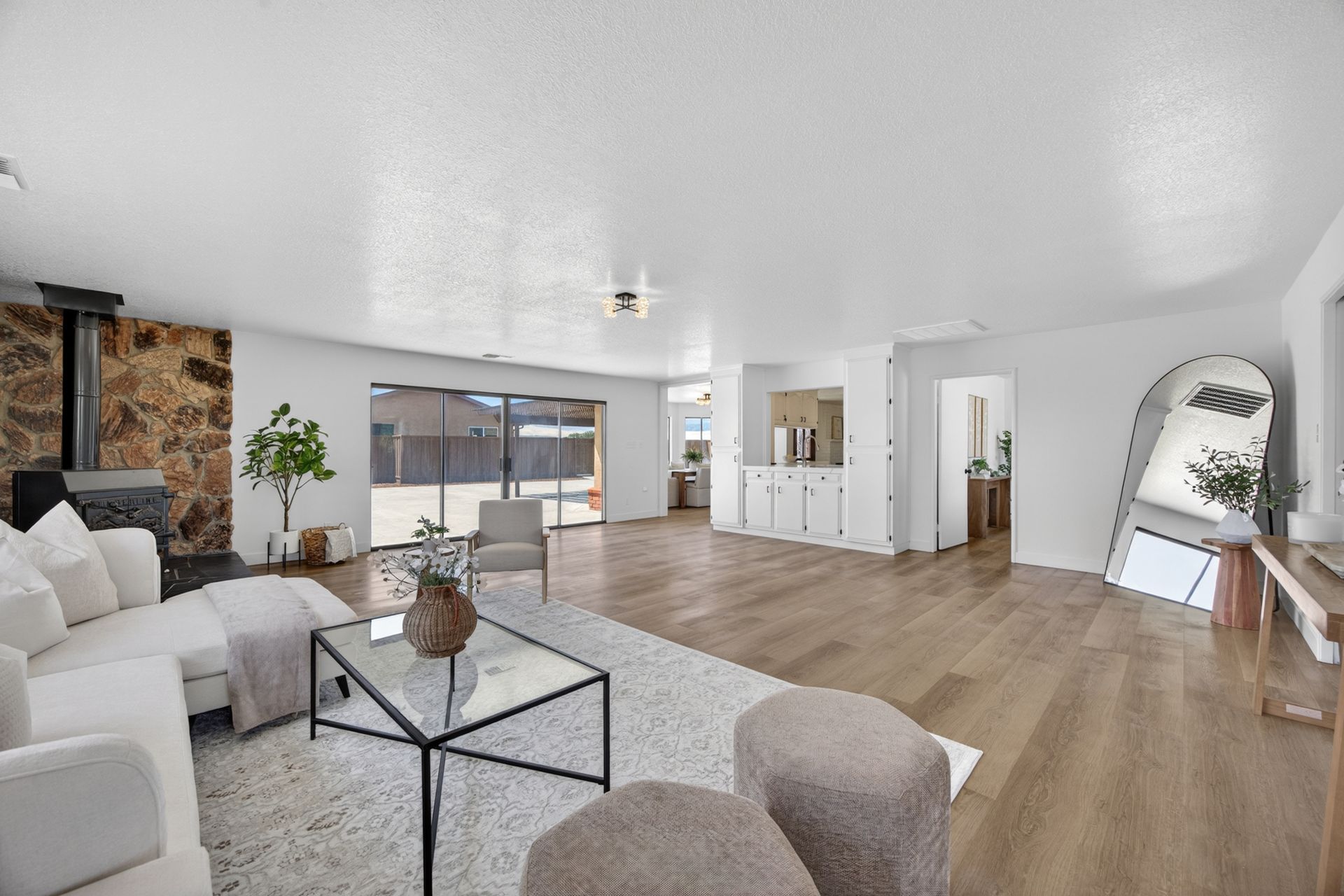 Open great room with a stone-clad fireplace, wide plank floors, and sliding doors to the patio