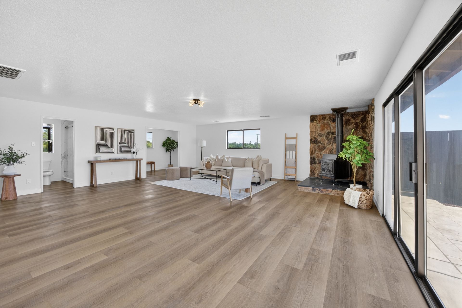 Secondary view of the great room with the stone fireplace, large windows, and pale sectional sofa