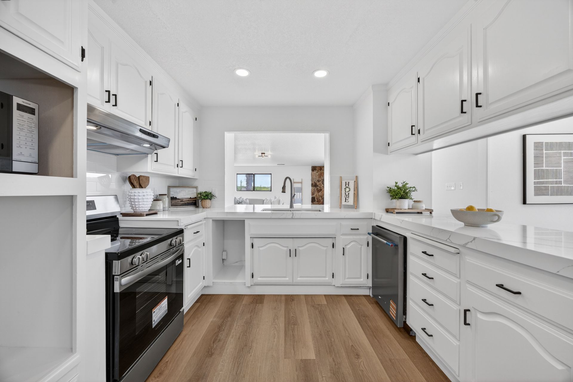 Updated kitchen with white cabinetry, quartz countertops, stainless range, and a pass-through to the dining area beyond