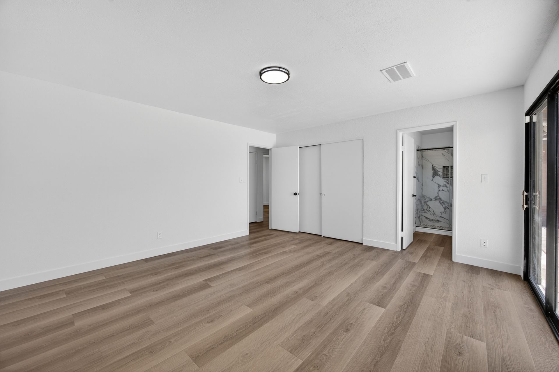 The primary suite with a wall of closets, a private bath beyond a side door, and warm plank flooring